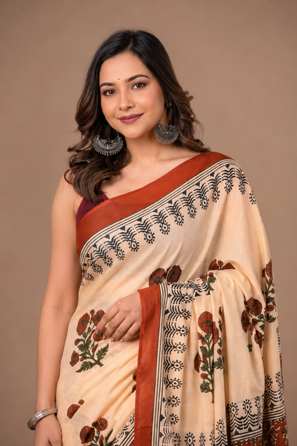 Cream floral cotton saree with a rust border and dark botanical detailing.
